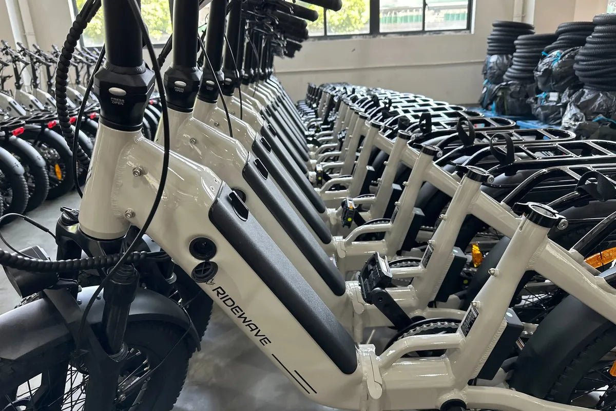 Row of warm grey Miniwave folding e-bikes lined up indoors, Ridewave logo on the down tube