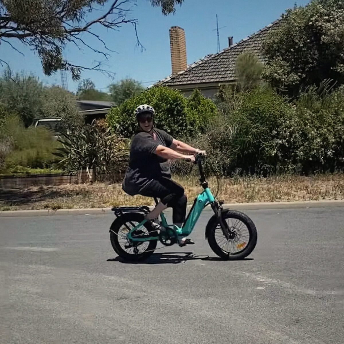 A rider on an aqua Ridewave Miniwave folding e-bike on a sunny street