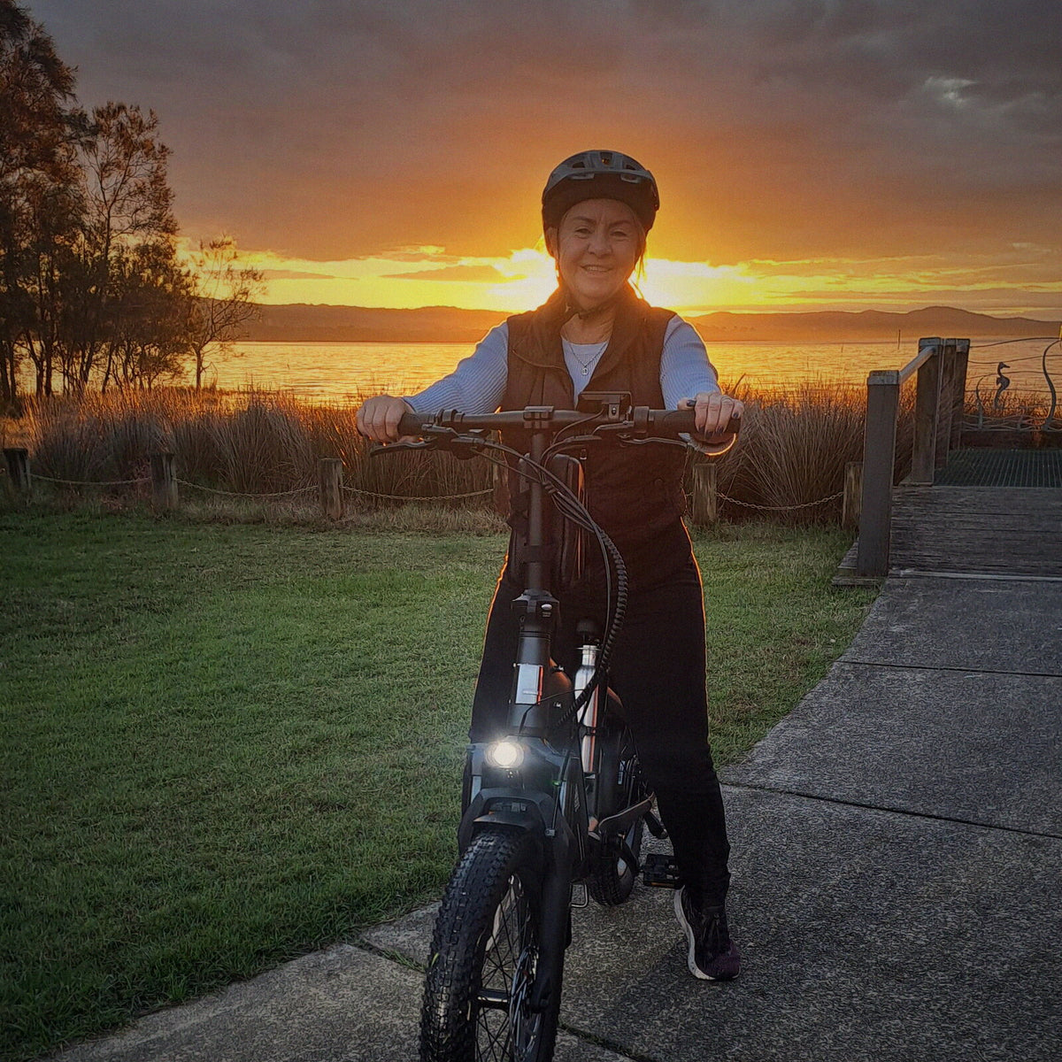 A rider in a helmet on a Ridewave Miniwave folding e-bike by the water at sunset