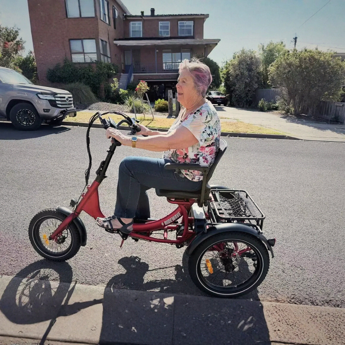 Rider on a red Ridewave Platypus electric trike on a sunny suburban street
