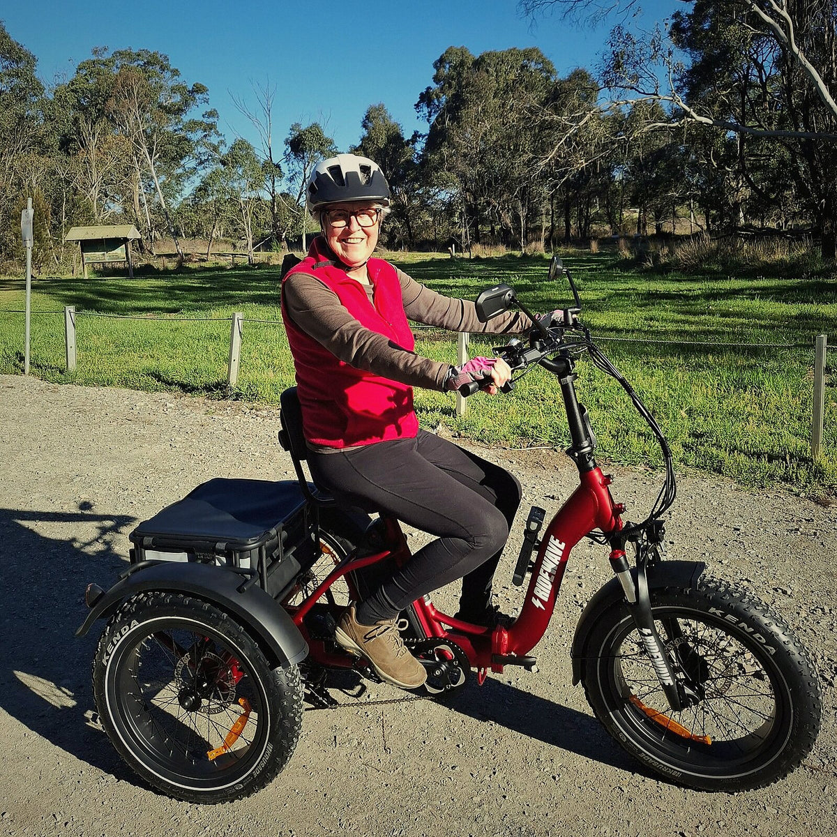 A Ridewave rider on a red Wallaby Plus electric trike on a gravel path among gum trees