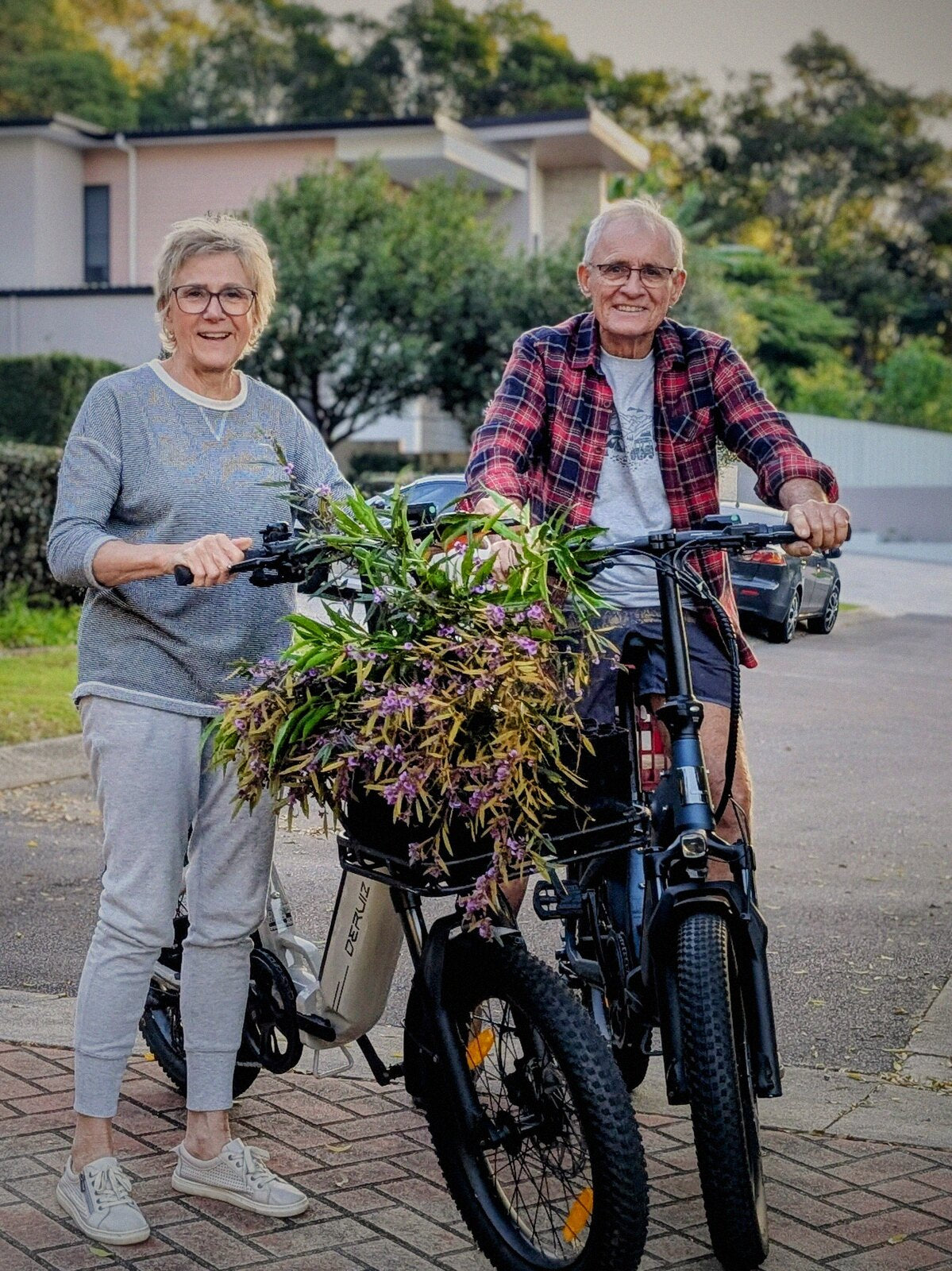 A smiling couple with their two Ridewave Miniwave folding e-bikes, a bunch of plants in the basket